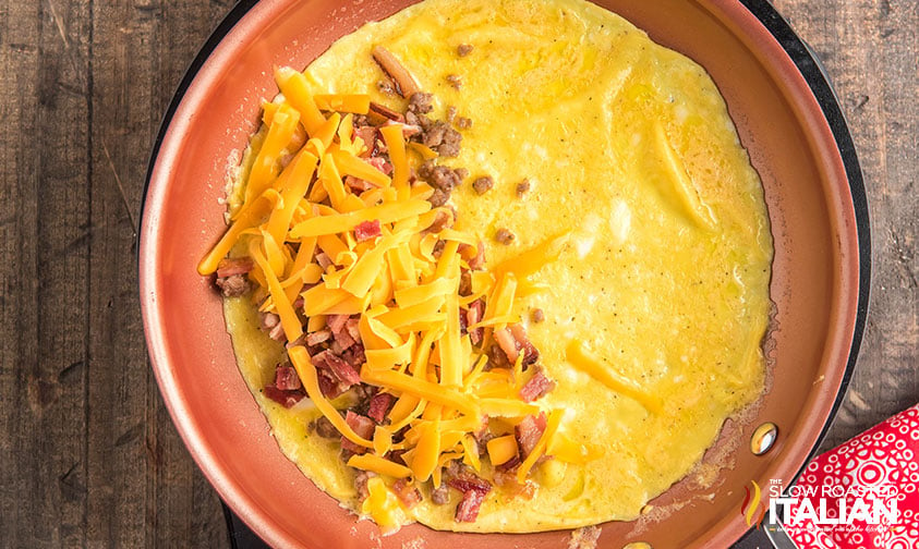 cheese, sausage and bacon added to omelette in a skillet