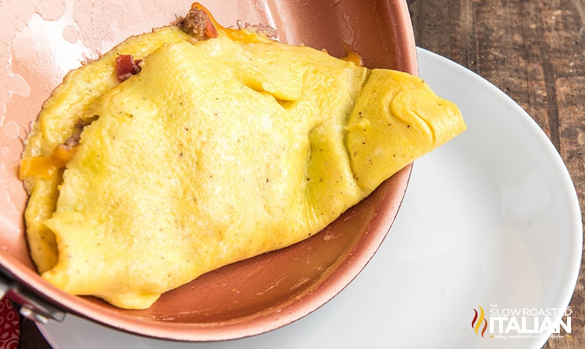 folded meat lovers omelette sliding from pan to plate