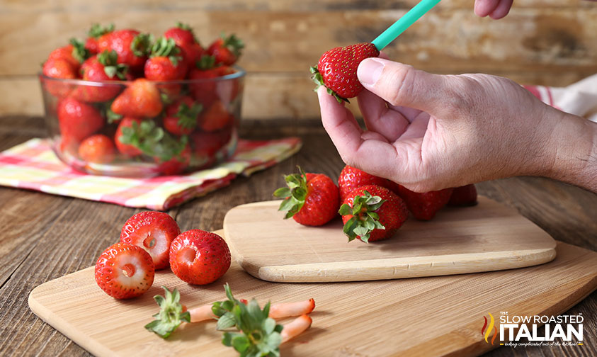 pushing a green straw through a strawberry