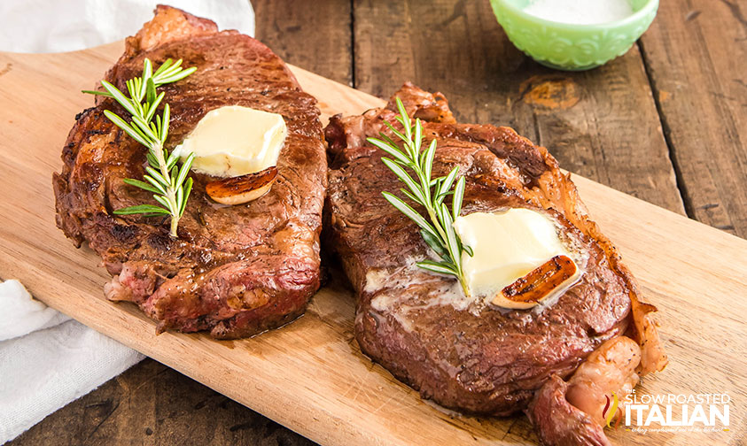 two cast iron ribeye steaks on a cutting board