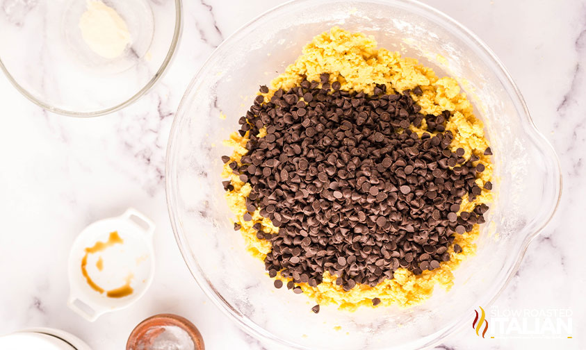 adding chocolate chips to cookie dough in a large mixing bowl