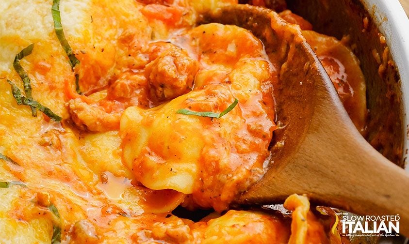 closeup: wooden spoon in skillet of cheesy ravioli and sauce