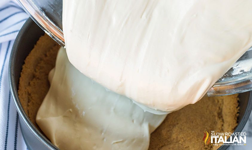 pouring cheesecake batter over graham cracker crust in springform pan