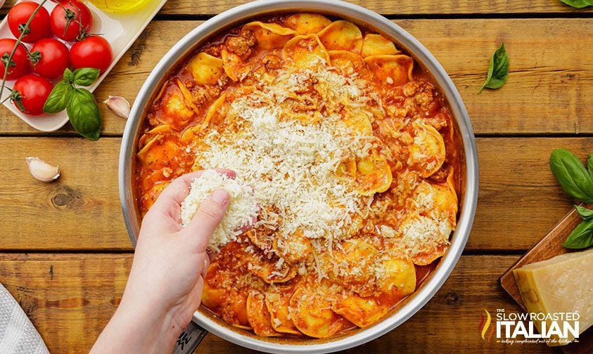 sprinkling shredded cheese over skillet ravioli