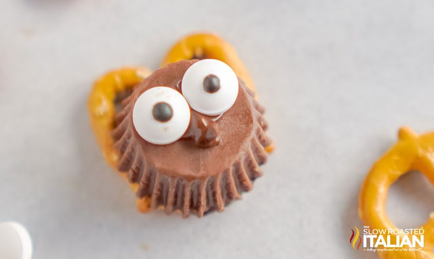 candy eyes stuck to the bottom of a reese's cup on top of a pretzel