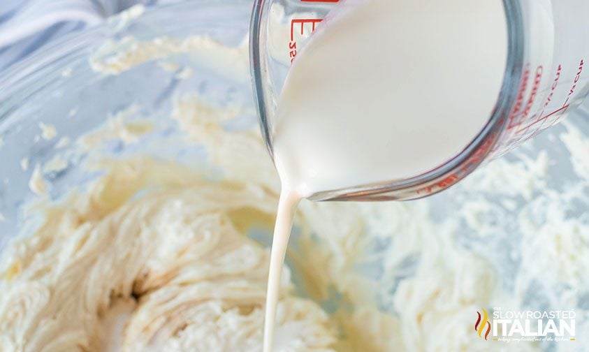 pouring heavy cream from a measuring cup into a bowl of cheesecake batter