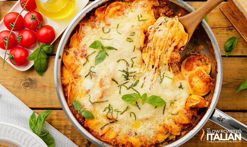 scooping out one pot ravioli topped with melted cheese and fresh basil