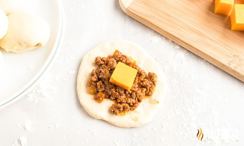 flatted circle of dough topped with sloppy joe filling and a cube of cheddar cheese