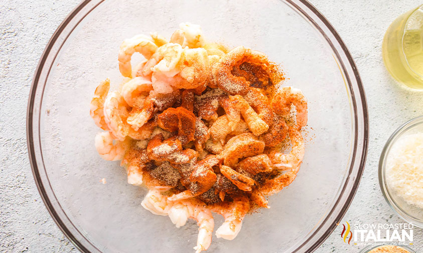 shrimp in a mixing bowl coated in butter and olive oil and sprinkled with seasoning