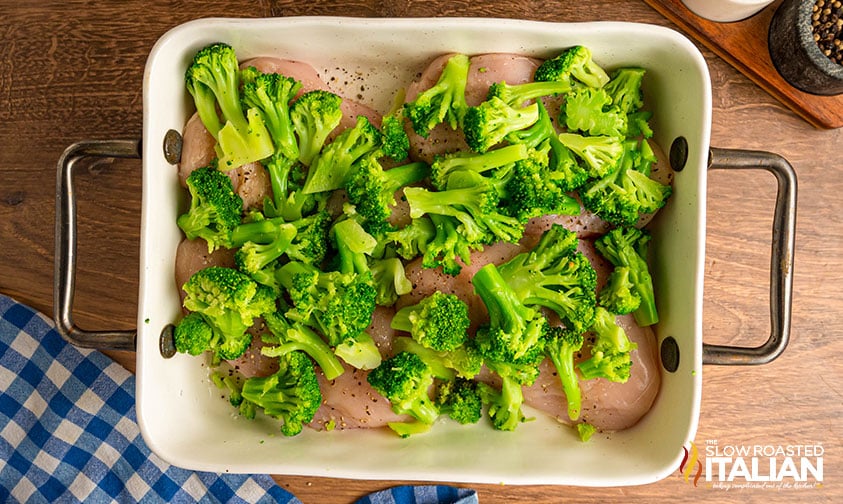 broccoli added to seasoned chicken breasts in a baking dish