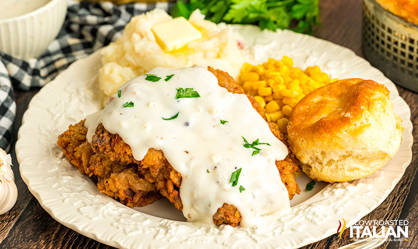 copycat cracker barrel country fried steak on a plate with mashed potatoes, corn and a biscuit