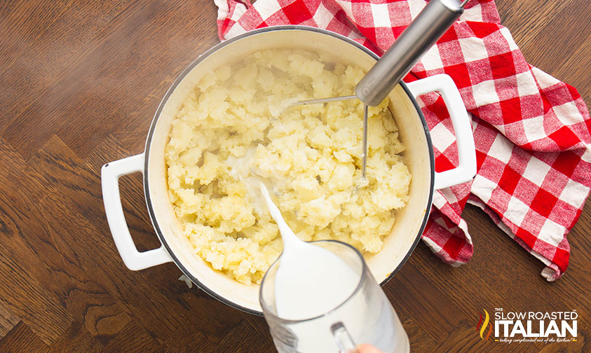 adding milk to mashed potatoes in a large pot