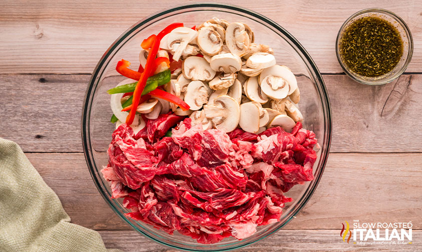 ribeye steak slices, bell peppers, onions, and mushrooms in a large bowl