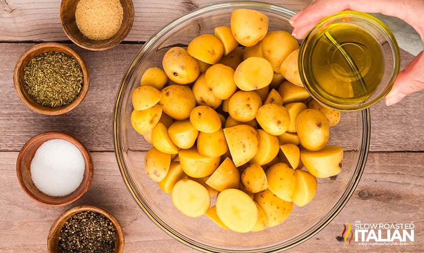 adding oil and seasoning to sliced potatoes in a bowl