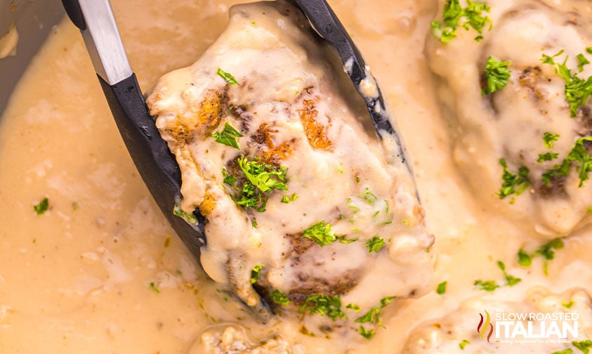 using tongs to lift up a smothered chicken breast