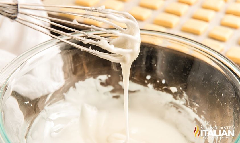 cookie icing drizzling off whisk into bowl