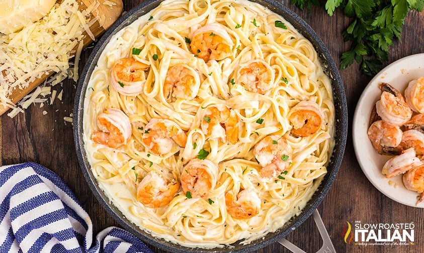 skillet of fettuccine alfredo topped with sauteed shrimp