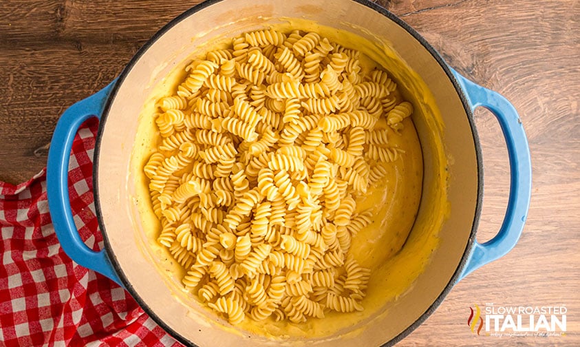 adding cooked pasta to cheese sauce in large pot