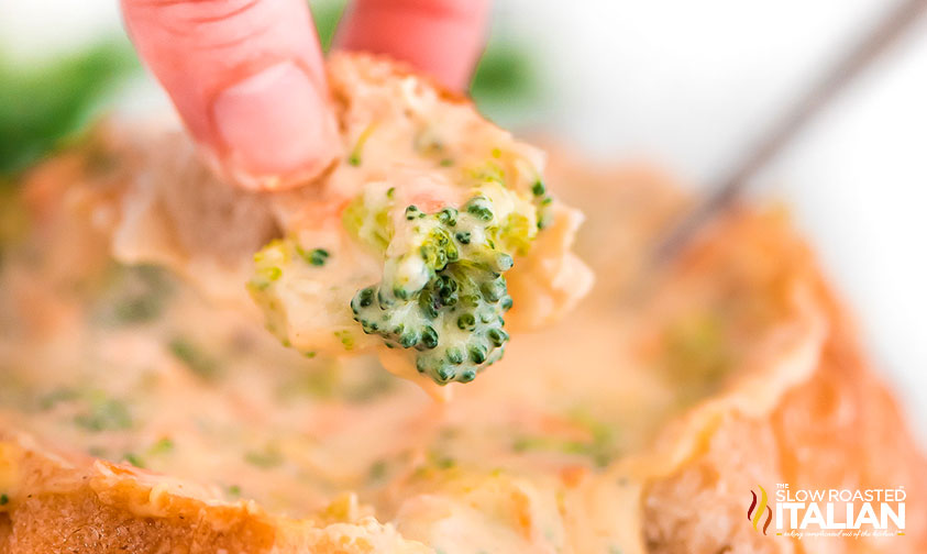 dipping a piece of bread into bread bowl of broccoli cheddar soup