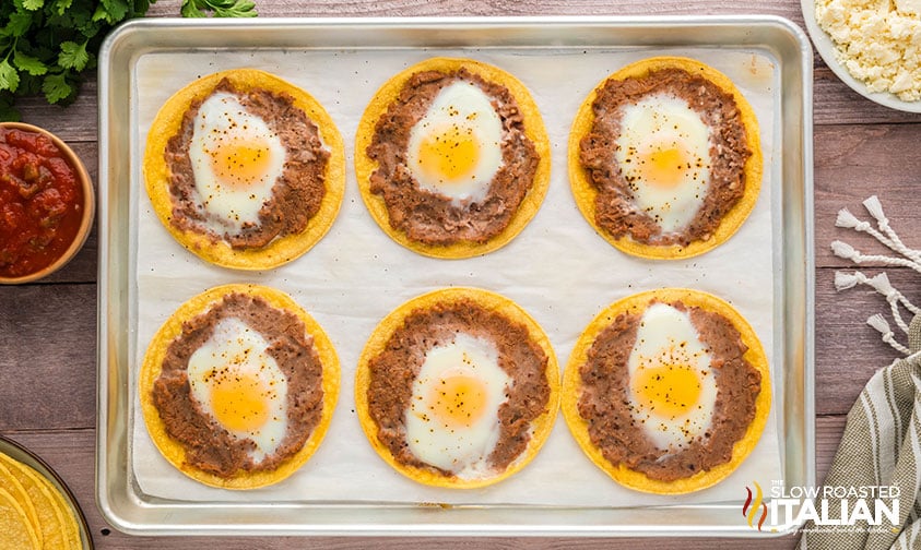 eggs cracked in center of refried beans on corn tortillas