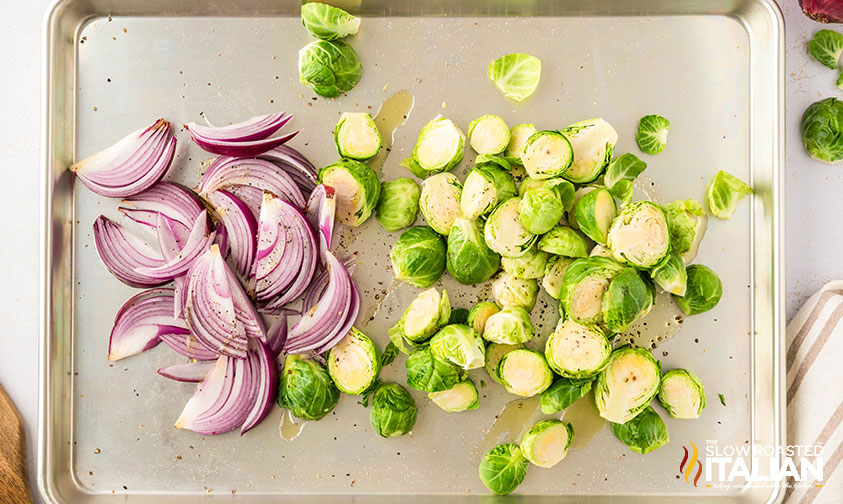 sliced brussels sprouts and onions seasoned on a baking sheet