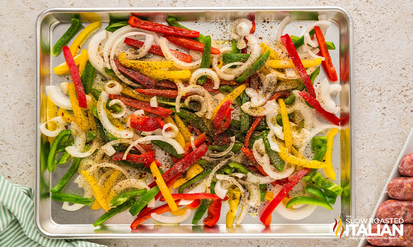 adding seasoning to sheet pan sausage and peppers