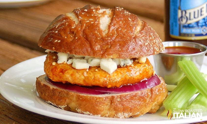 close up: spicy chicken burger plated with celery sticks and extra sauce, bottle of Blue Moon beer in the background