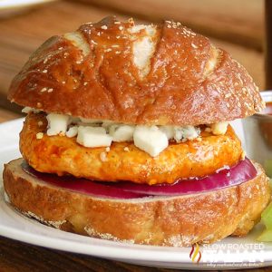 closeup of a spicy buffalo chicken burger in a bun with crumbled cheese and onion