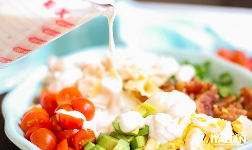 pouring dressing from measuring cup over chopped salad ingredients