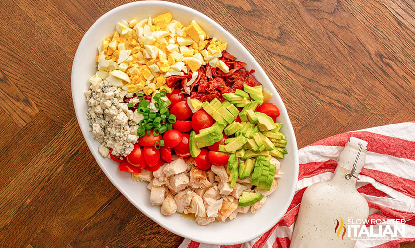 cobb pasta salad ingredients arranged in an oval bowl next to a bottle of creamy dressing