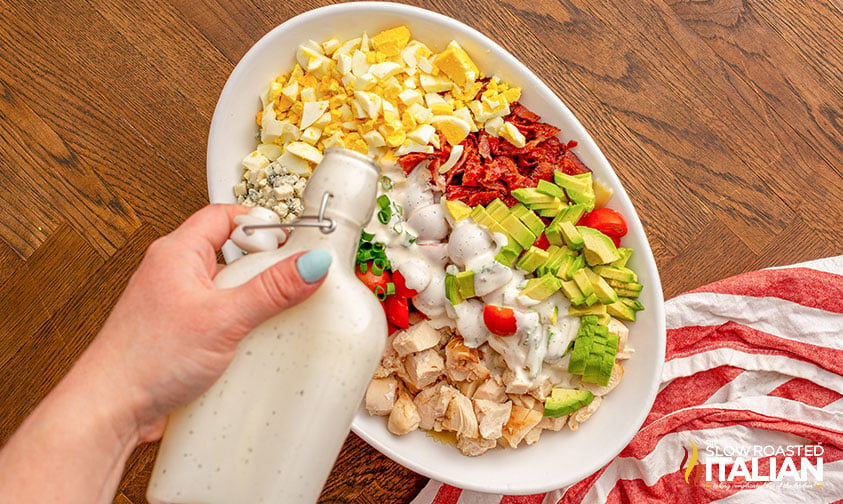 pouring creamy dressing over pasta salad ingredients