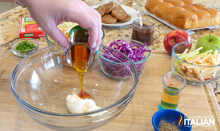 pouring honey into a large glass bowl with mayonnaise